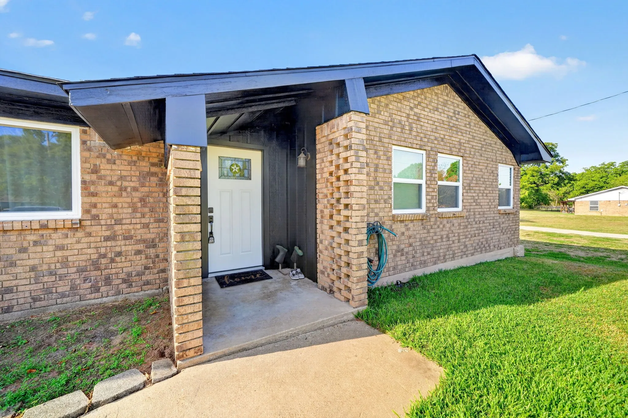 Brick exterior with white frame windows, an entryway porch, and a concrete walkway