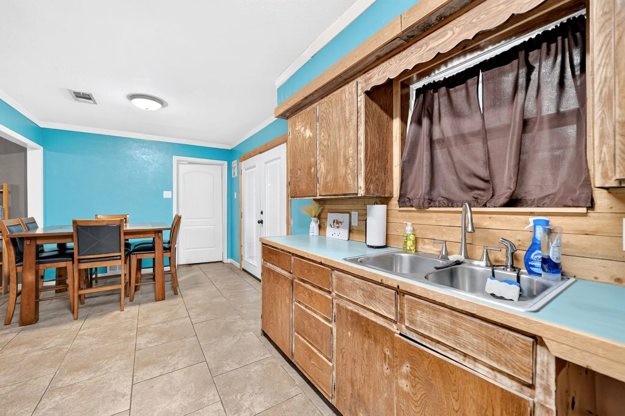 Kitchen area featuring wood-finish cabinetry, a double basin stainless steel sink, and light-colored tile flooring