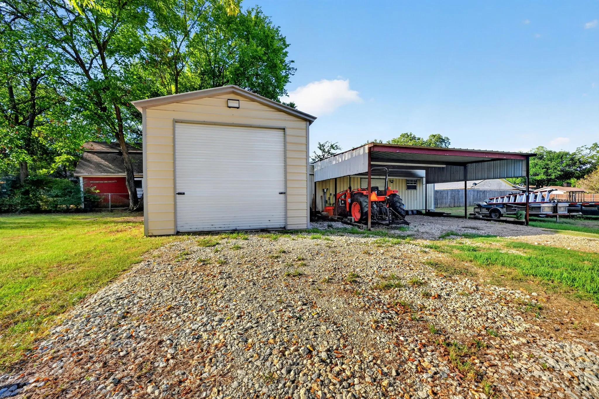 Detached garage with a roll-up door, gravel driveway, and a large metal carport structure