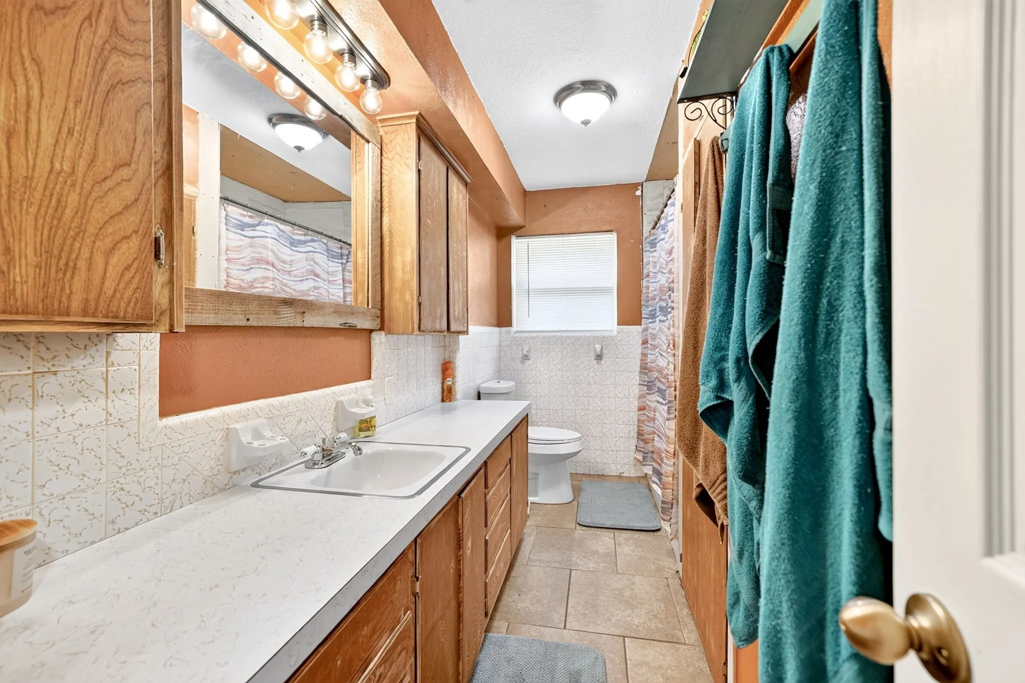 Extended vanity with wood-finish cabinetry, tile flooring, and a window