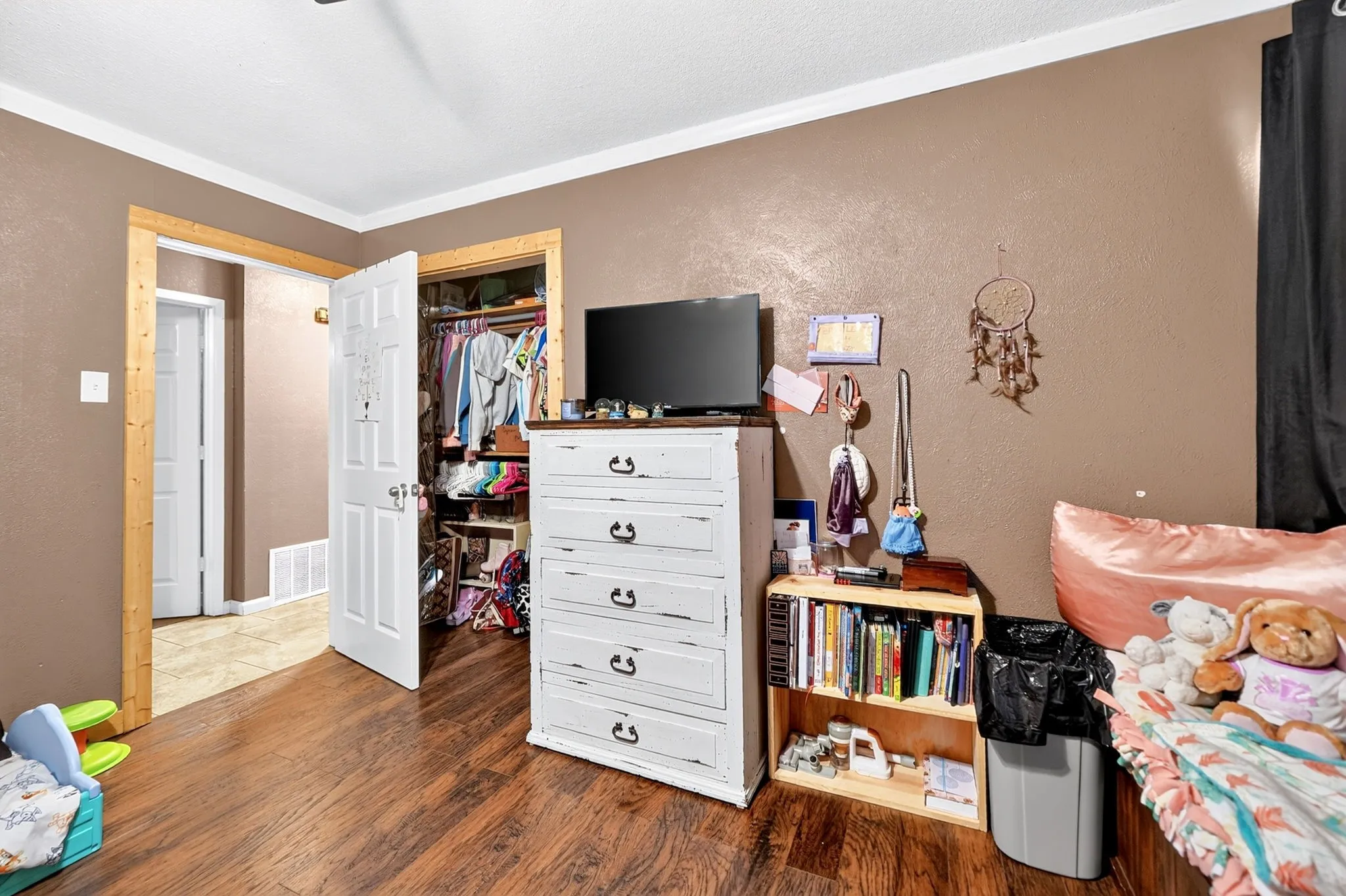 Wood-finish flooring throughout, white trim, and a built-in closet with shelving and hanging rods