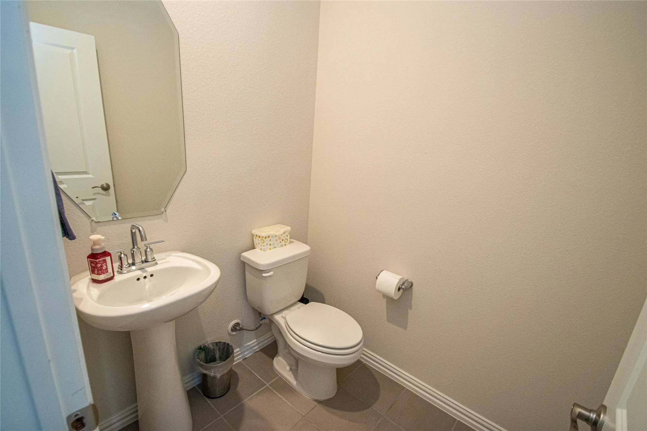 Pedestal sink with chrome faucet, beveled wall mirror, white toilet, and gray tile flooring