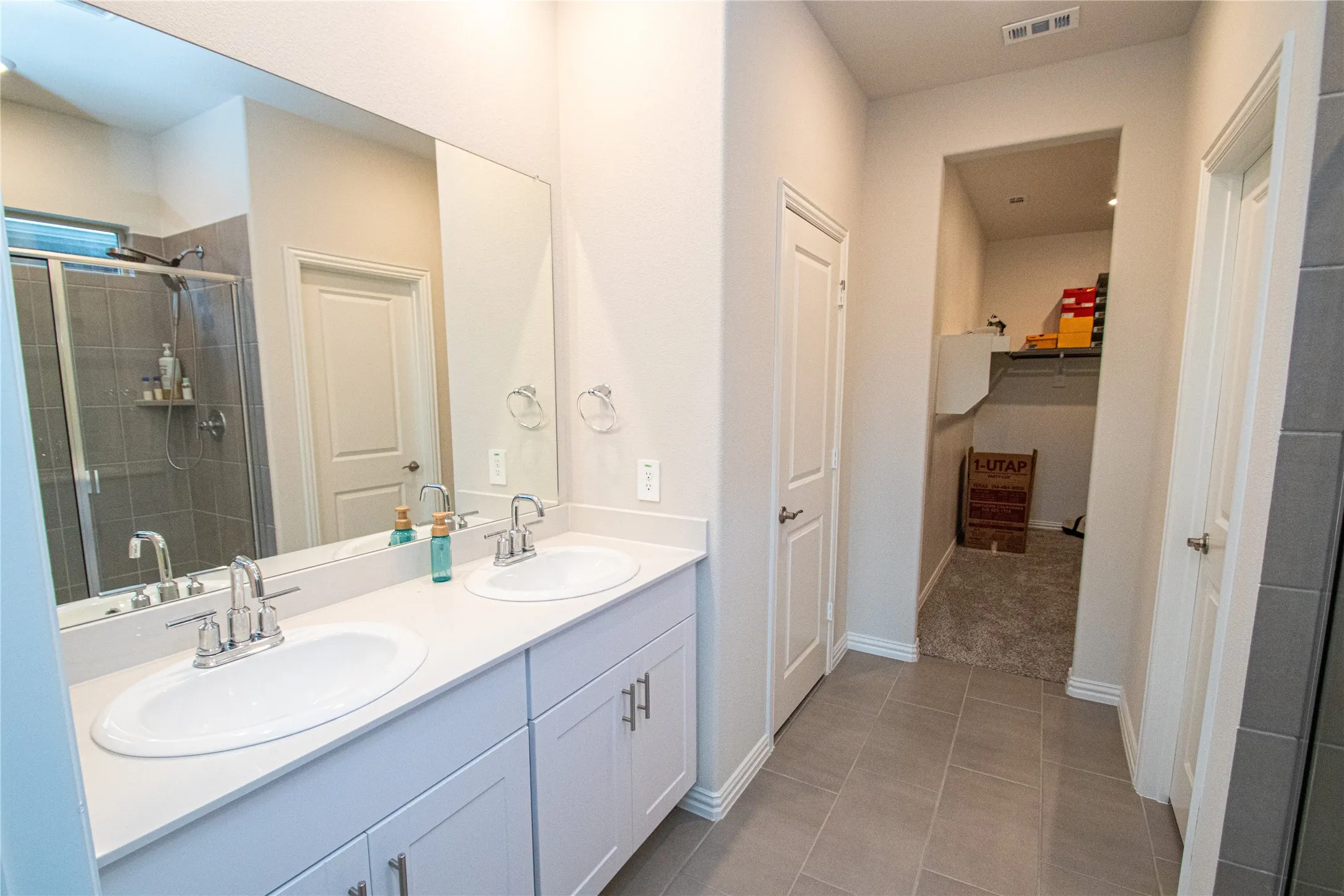 Dual sink vanity with white cabinetry and chrome fixtures, large mirror, tile flooring, and walk-in closet with built-in shelving