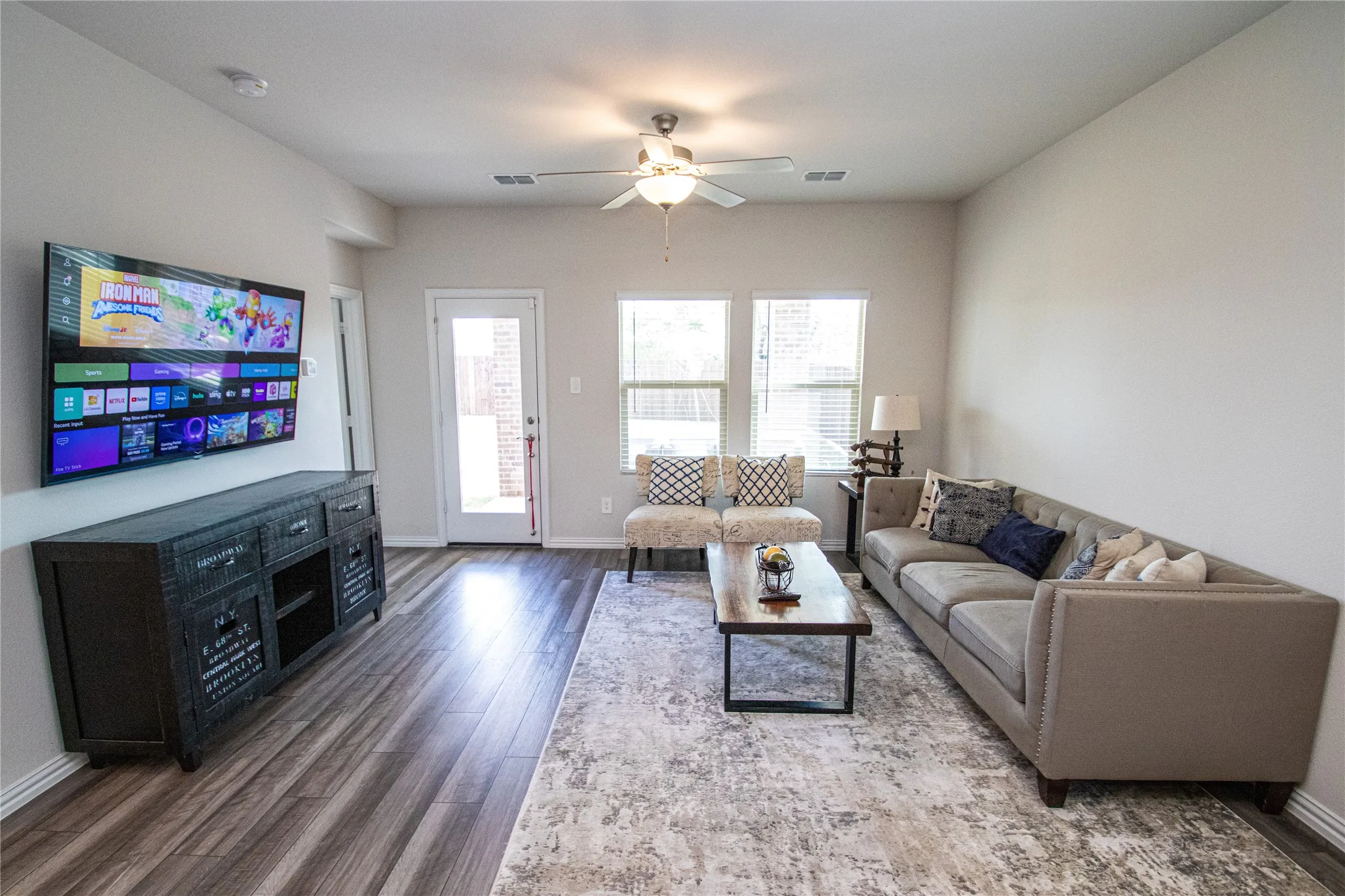 Wood-finish flooring throughout, multiple windows with blinds, ceiling fan, and a glass-paneled exterior door