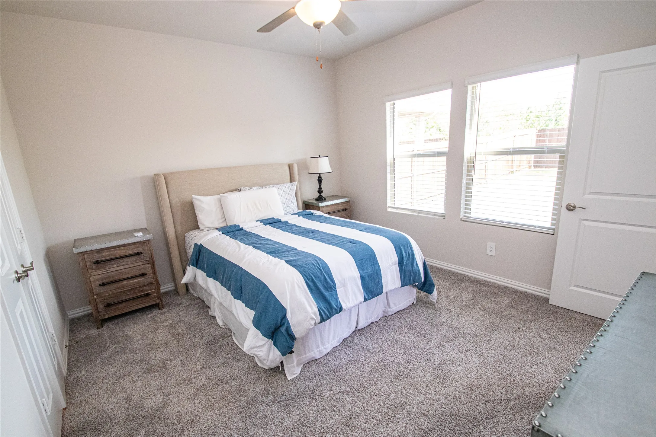 Vaulted ceiling, two windows with blinds, light gray carpet, ceiling fan, and white interior door