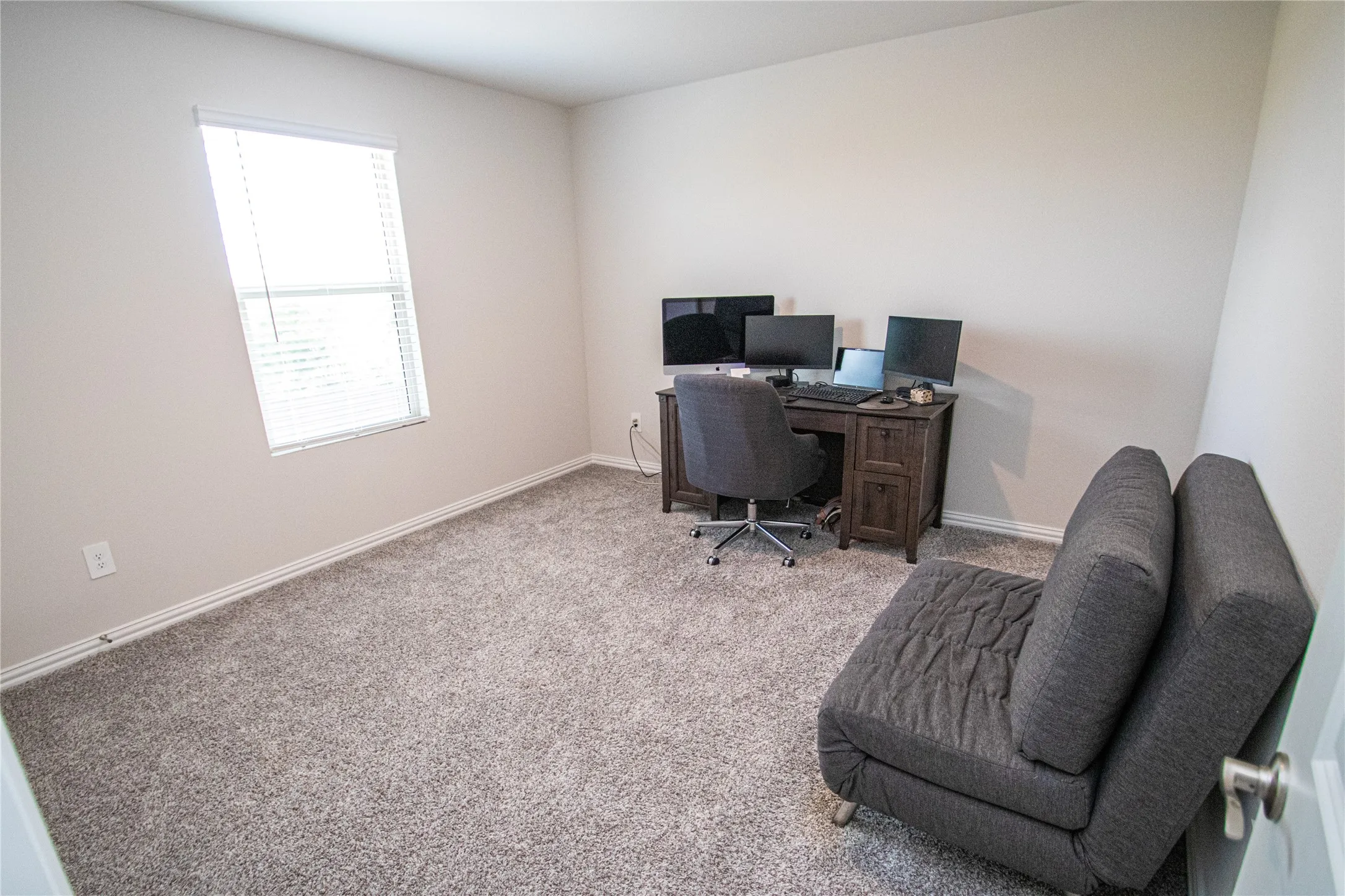 Neutral tone wall paint, light gray carpeting, and a single window with blinds
