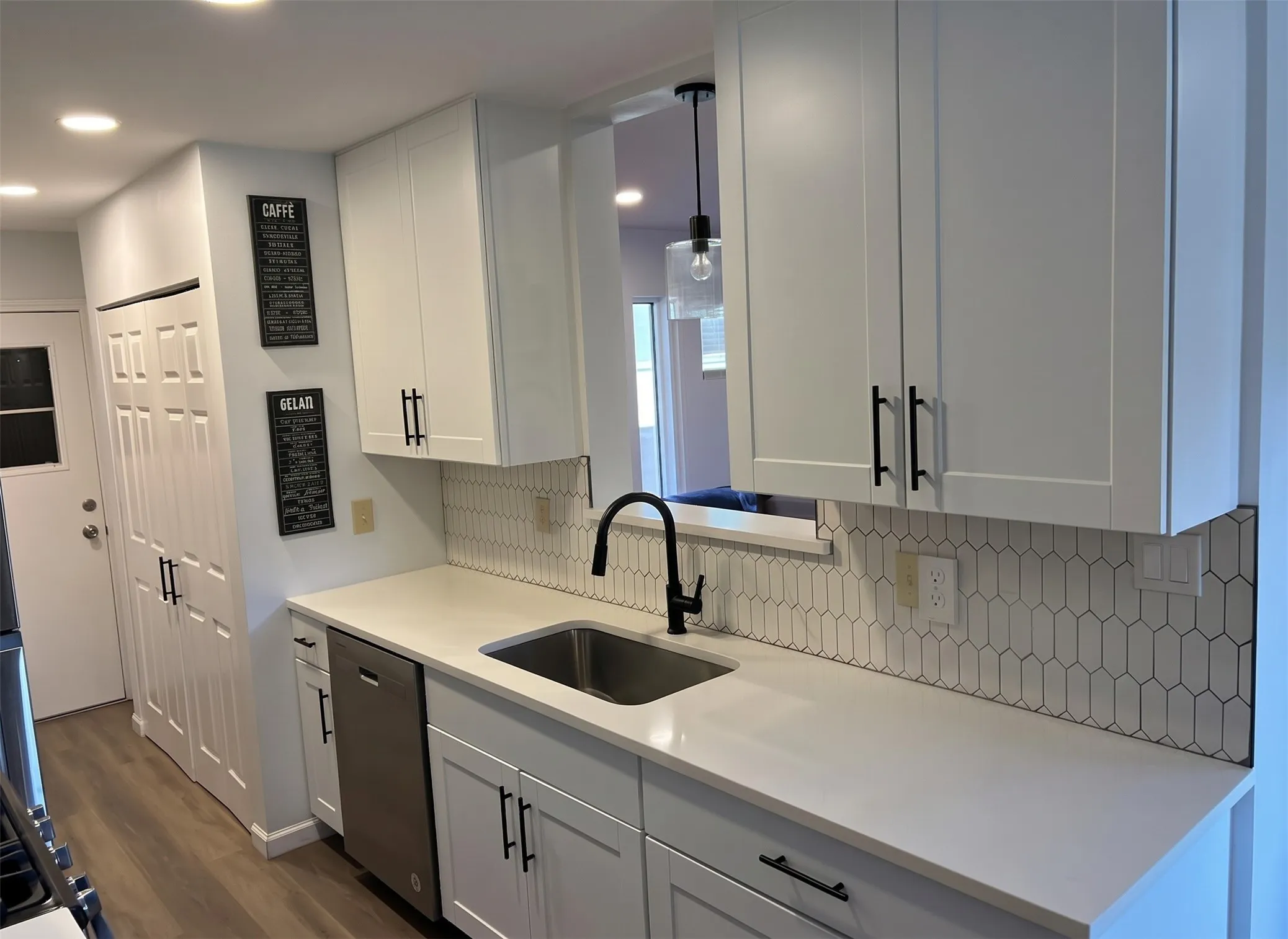White shaker-style cabinetry with matte black hardware, stainless steel sink with a matte black faucet, and white countertops