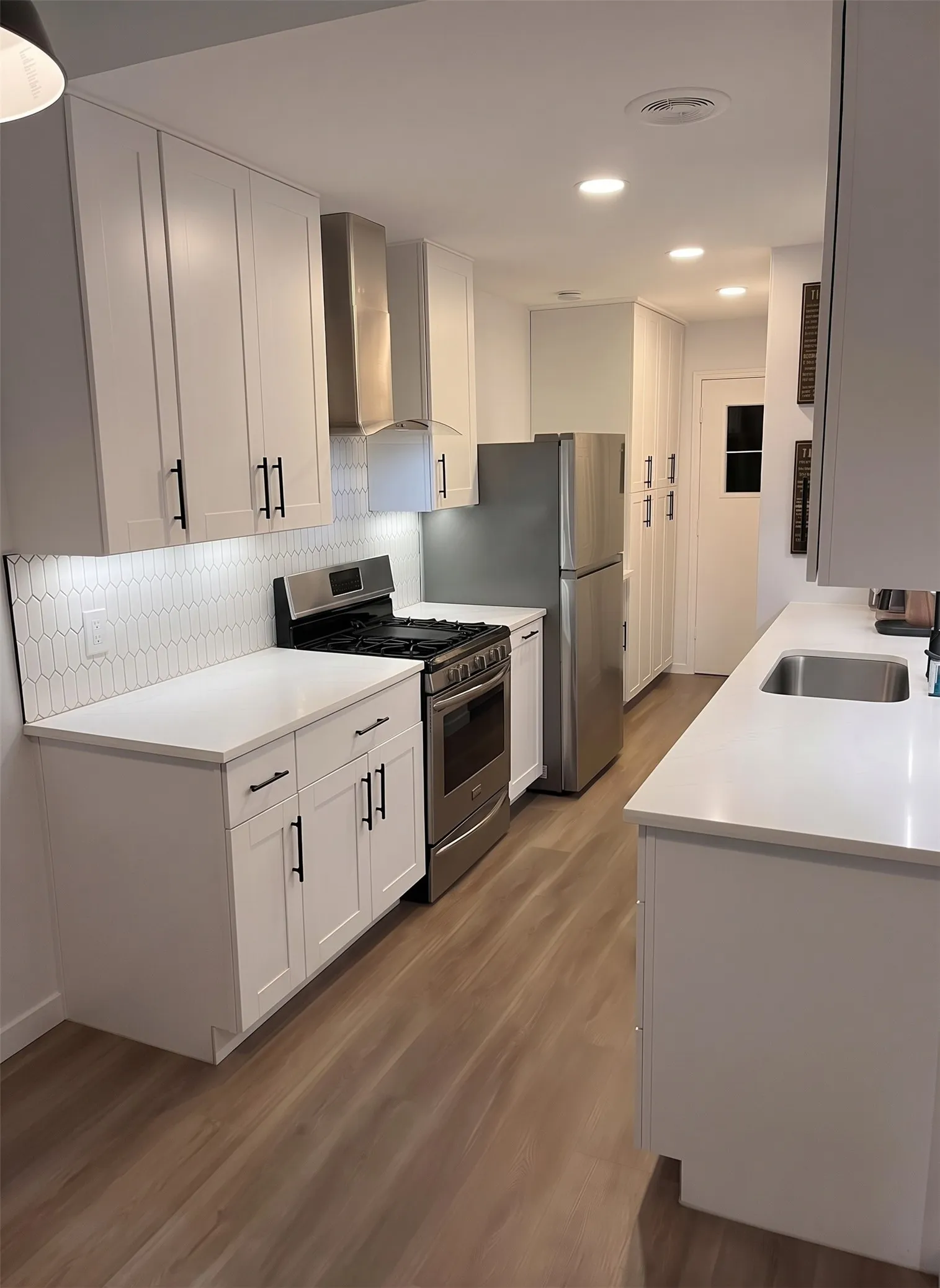 White shaker cabinetry with matte black hardware, stainless steel appliances, white quartz countertops, full subway tile backsplash, and wood-finish flooring