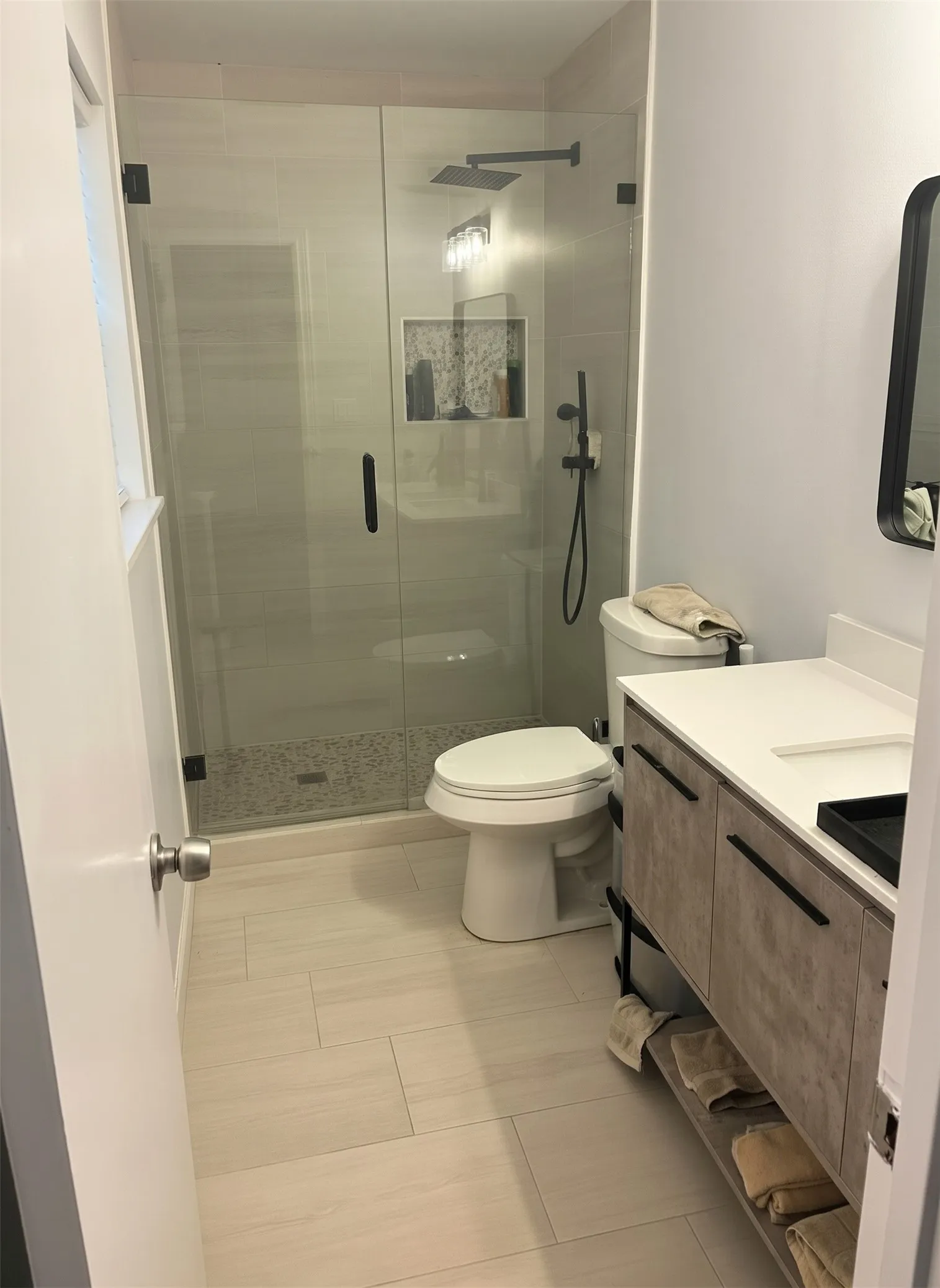 Glass-enclosed shower with a rainfall showerhead, shower niche, and matte black fixtures