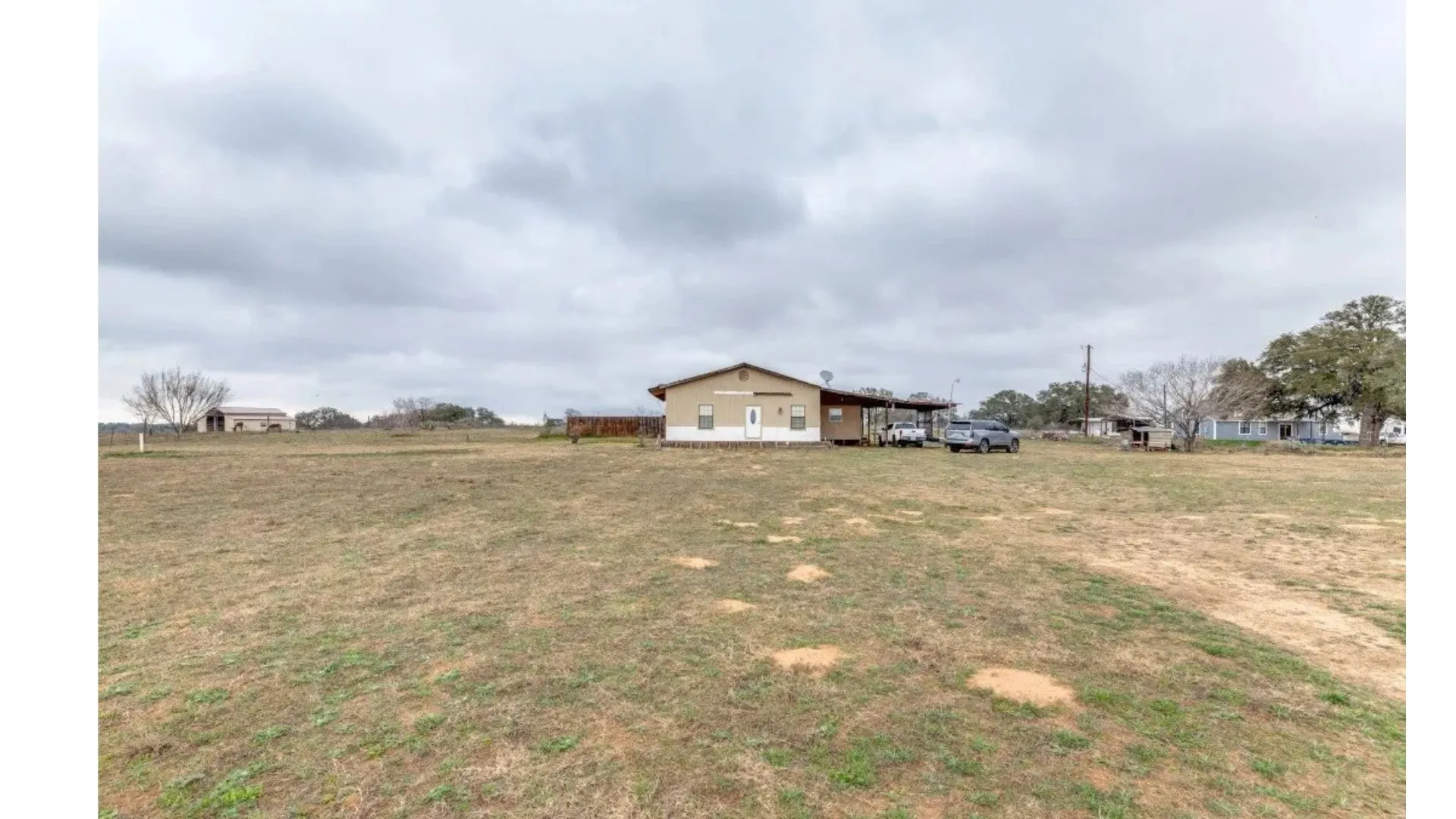 Expansive open land with a residential structure featuring a covered carport and a sloped roof