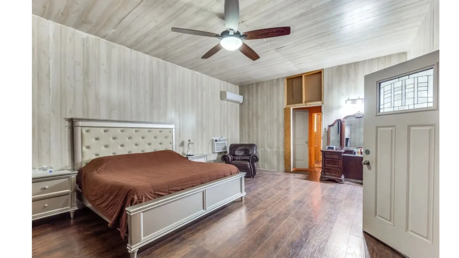 Wood-finish flooring, wood-paneled walls and ceiling, ceiling fan with integrated lighting, and a white paneled door with decorative glass insert