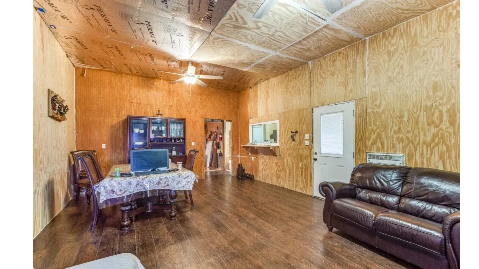 Wood-finish flooring throughout, plywood paneling on walls and ceiling, ceiling fan with light fixture, built-in display cabinetry, white exterior-style door