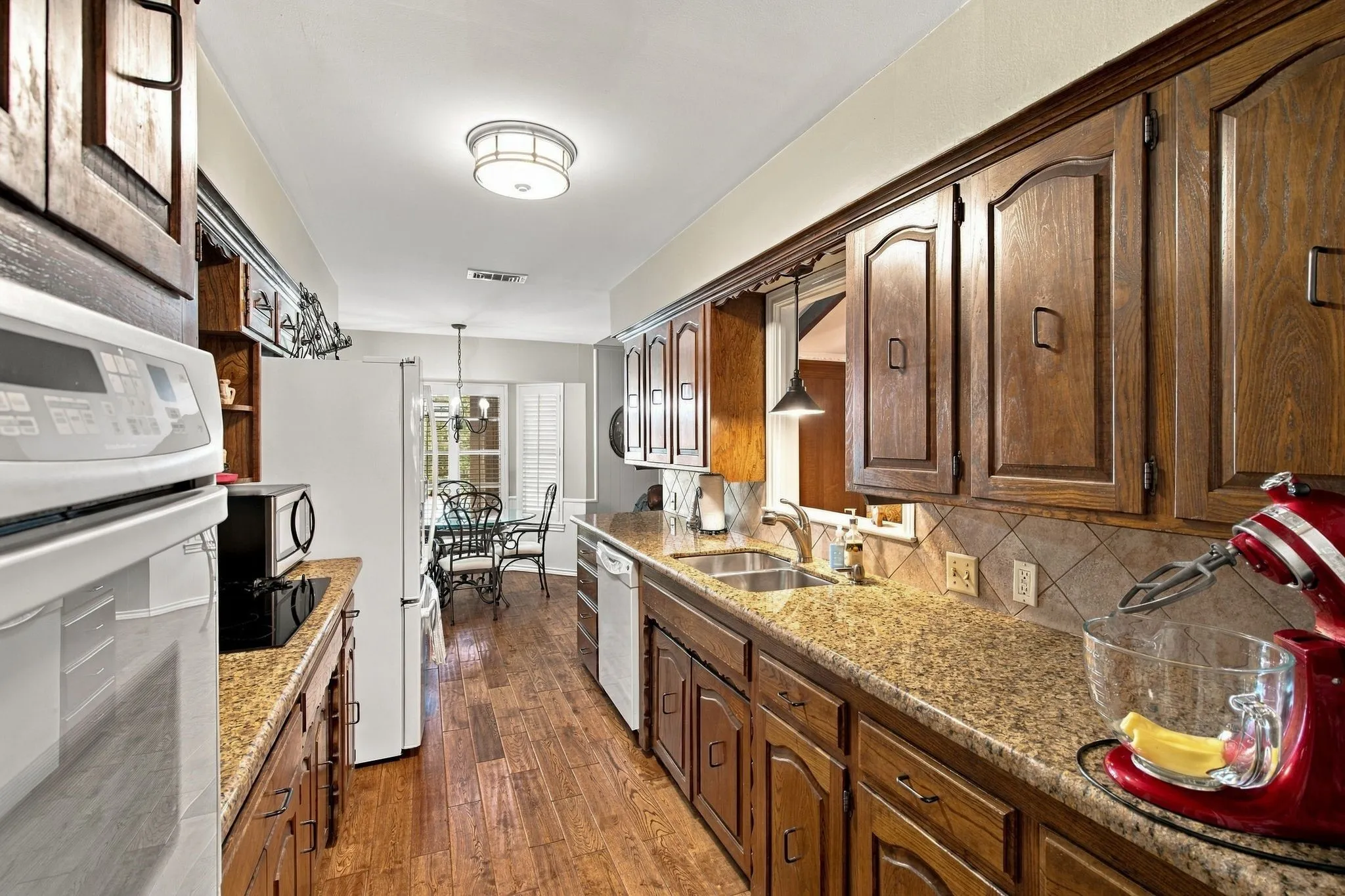 Galley kitchen featuring wood-finish cabinetry, granite-style countertops, and a tile backsplash