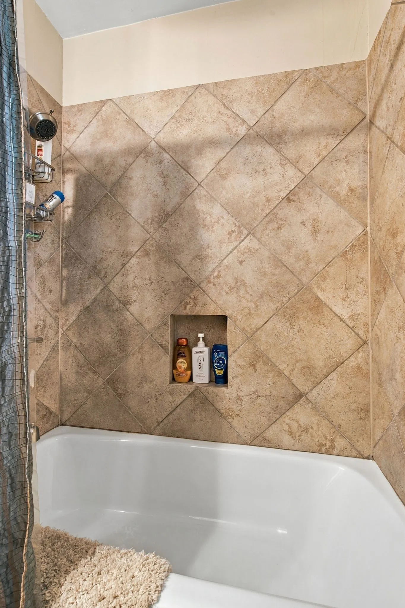 Bathtub with diagonally set wall tile, built-in shower niche, and a wall-mounted shower fixture