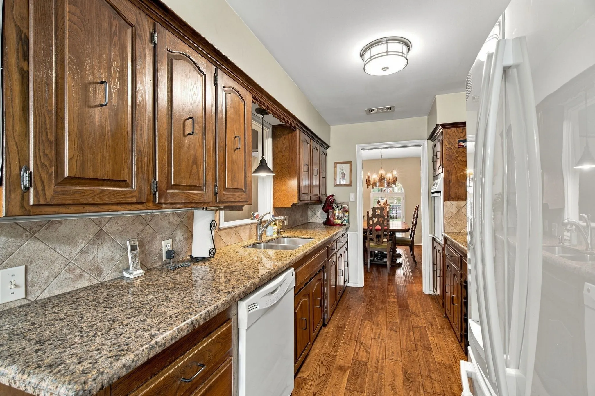 Kitchen featuring wood-finish cabinetry, granite countertops, tile backsplash, stainless steel sink, and wood-finish flooring