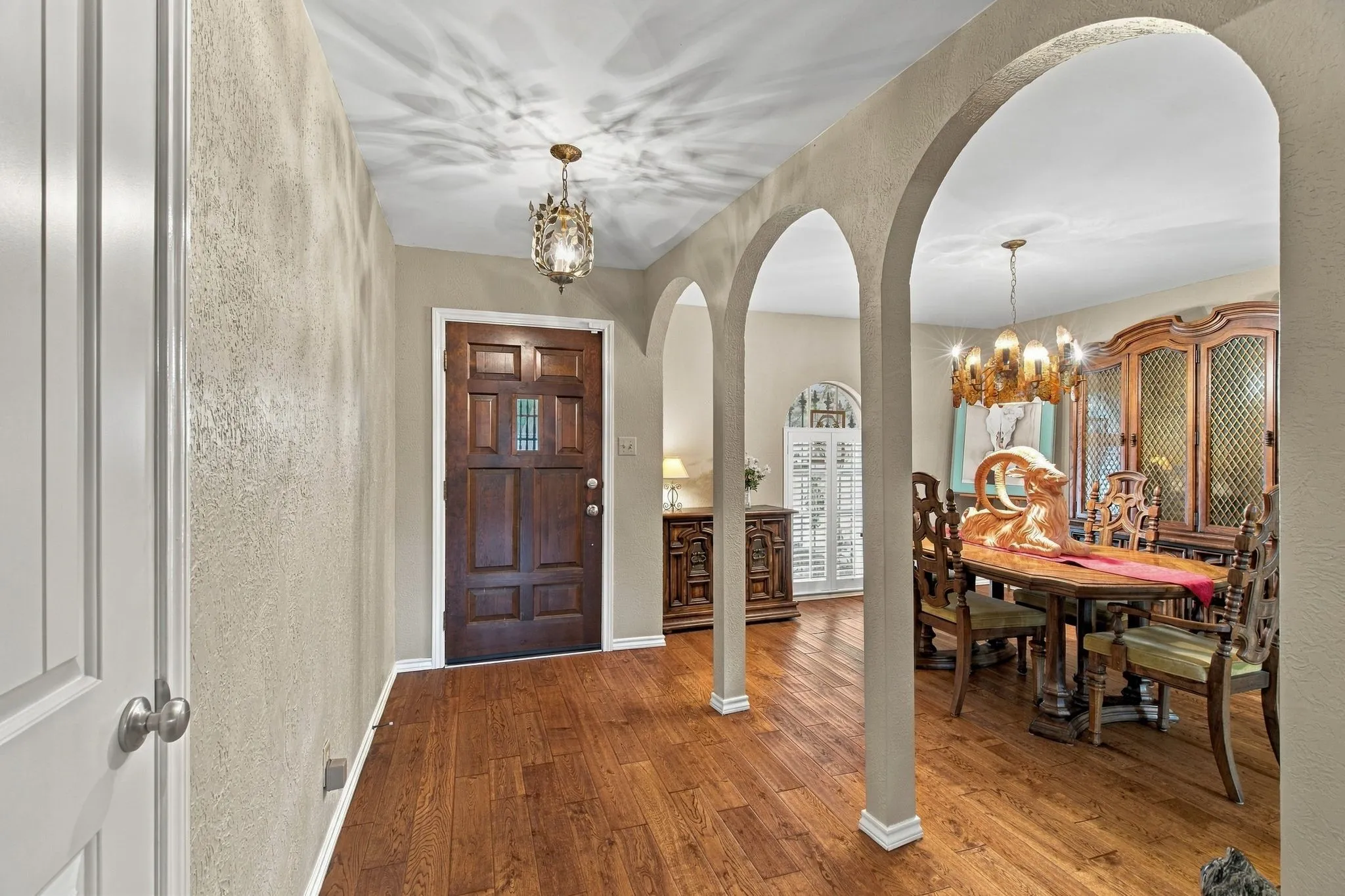 Hardwood-style flooring throughout, arched entryway, panel front door with leaded glass insert, and decorative ceiling fixture