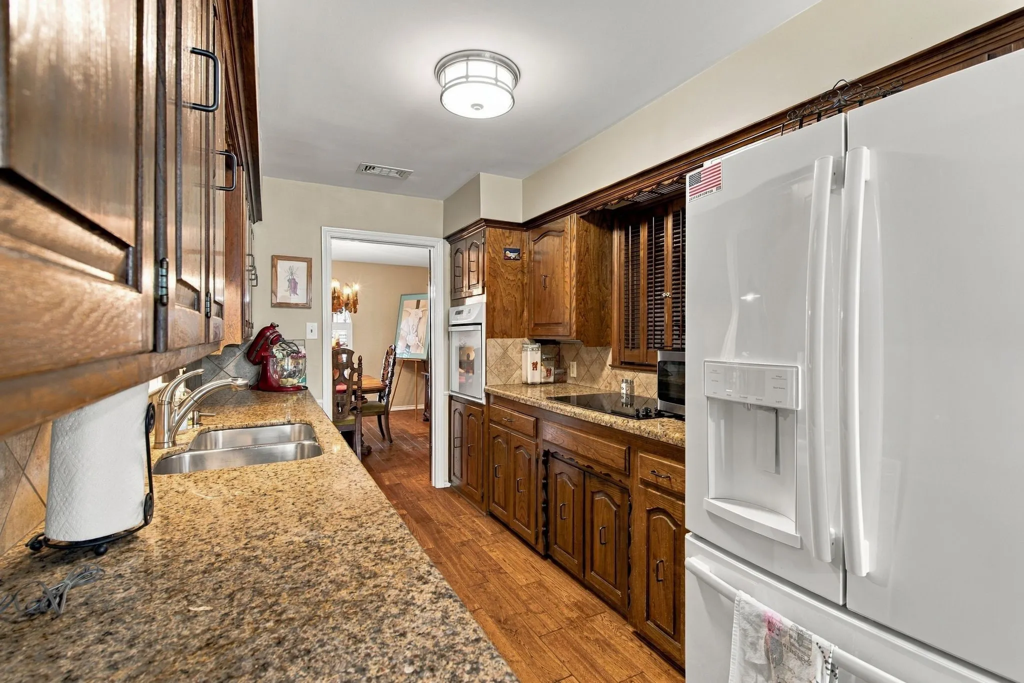 Kitchen featuring wood-finish flooring, stone-finish countertops, wood cabinetry, a stainless steel double sink, and a built-in cooktop