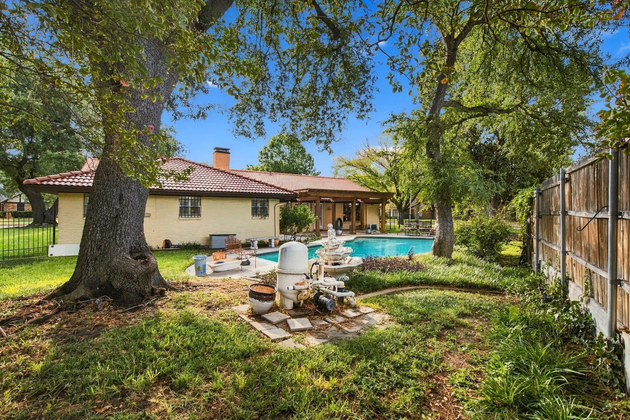 Expansive backyard featuring a swimming pool, mature trees, and a wooden privacy fence