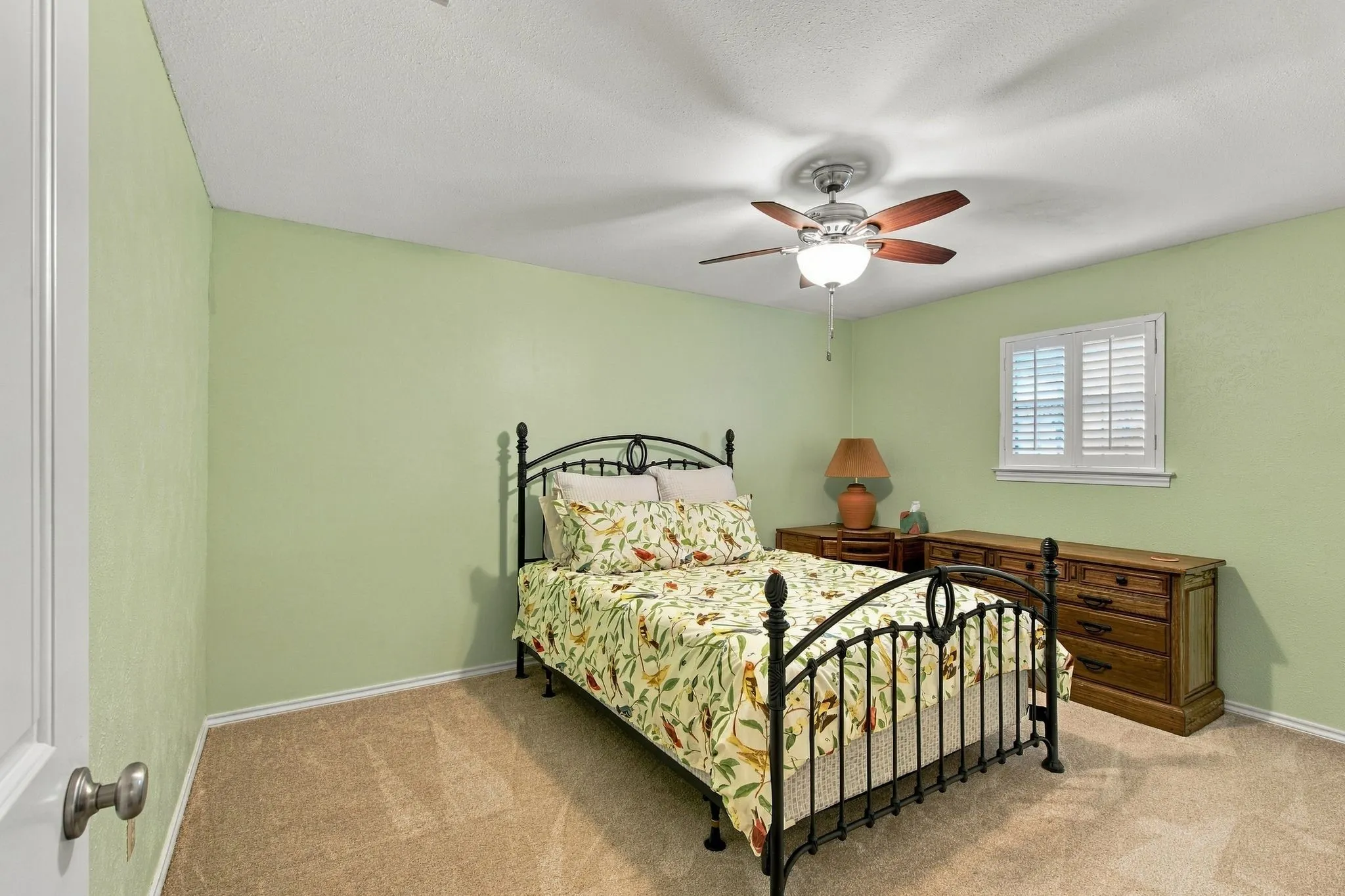 Carpeted room with a ceiling fan light fixture, a window featuring white plantation shutters, and light green wall paint