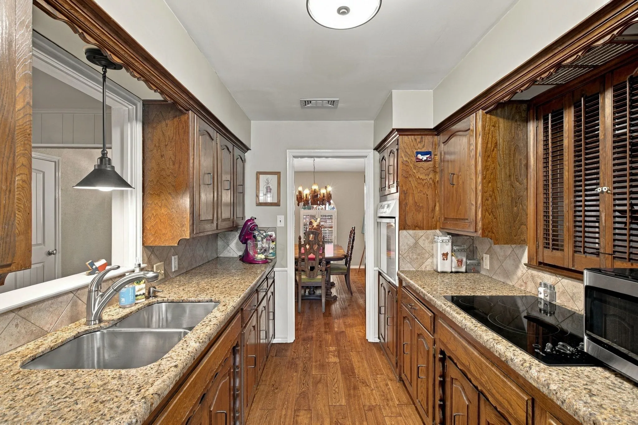 Galley kitchen featuring wood-finish flooring, wood cabinetry, stone countertops, and a double basin stainless steel sink