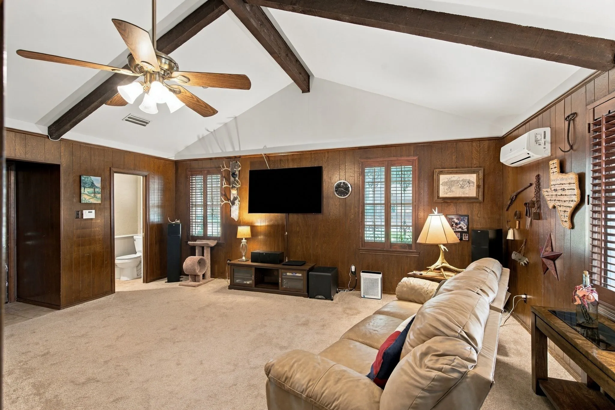 Vaulted ceiling with exposed wood beams, wood paneling, ceiling fan, and two windows with wood shutters
