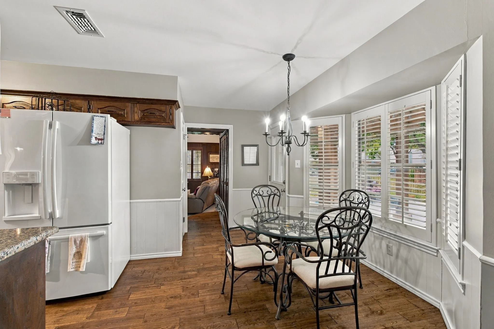 Wood-finish flooring with a bay window featuring plantation shutters and a chandelier