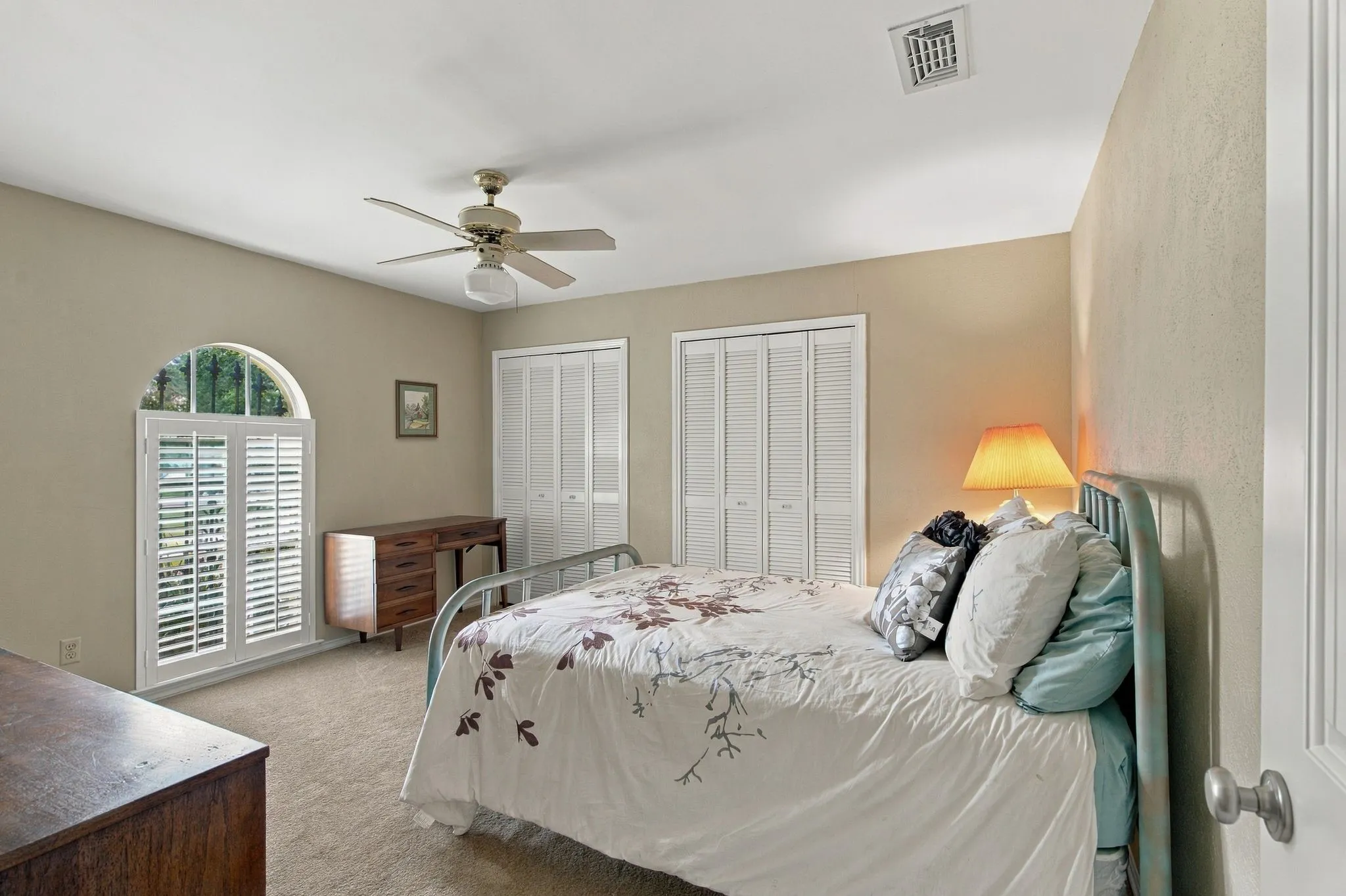 Arched window with plantation shutters, ceiling fan with integrated lighting, and two bi-fold closet doors