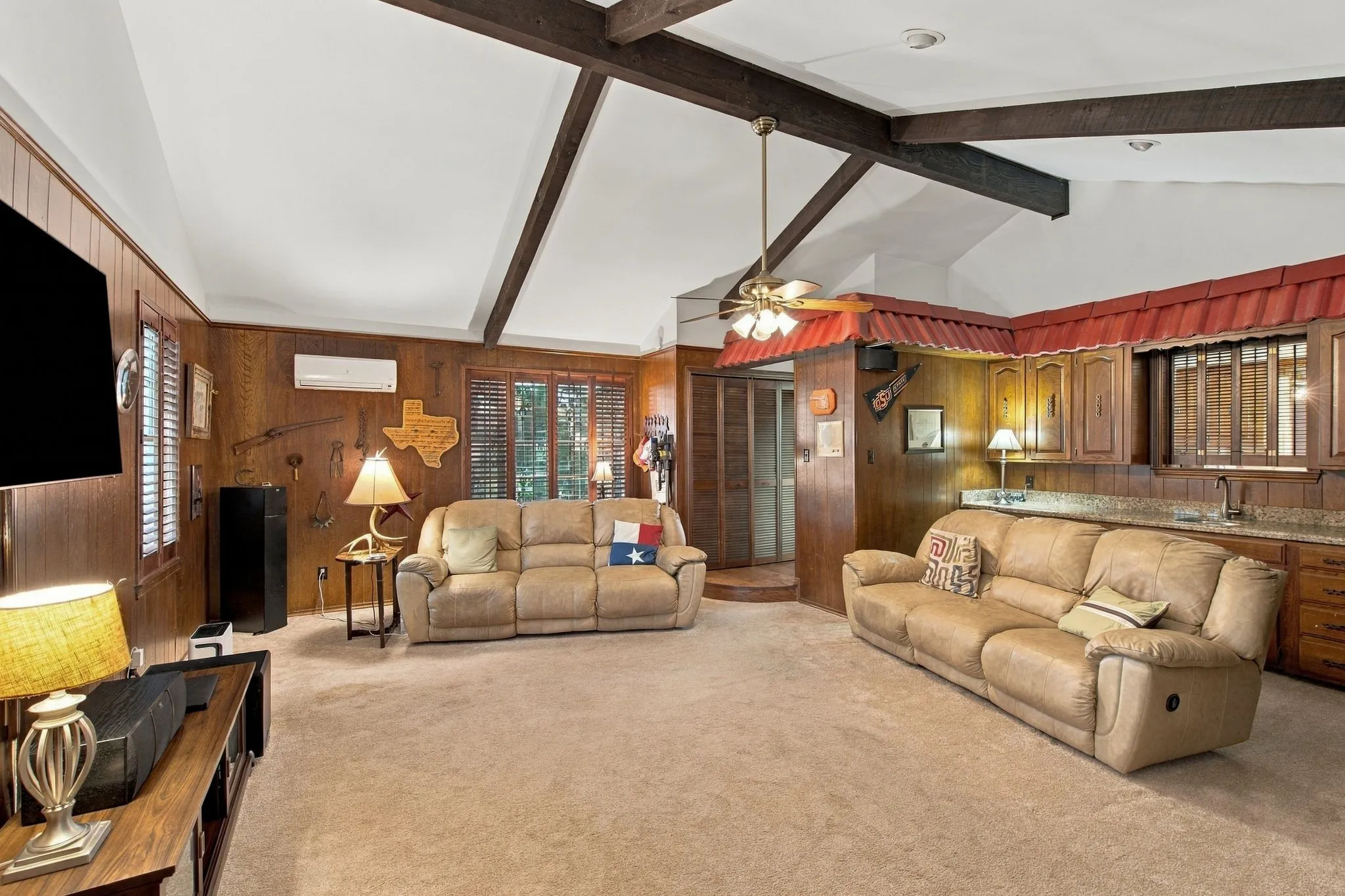 Vaulted ceiling with exposed wood beams, wood-paneled walls, built-in wet bar with wood cabinetry and countertop, and carpet flooring