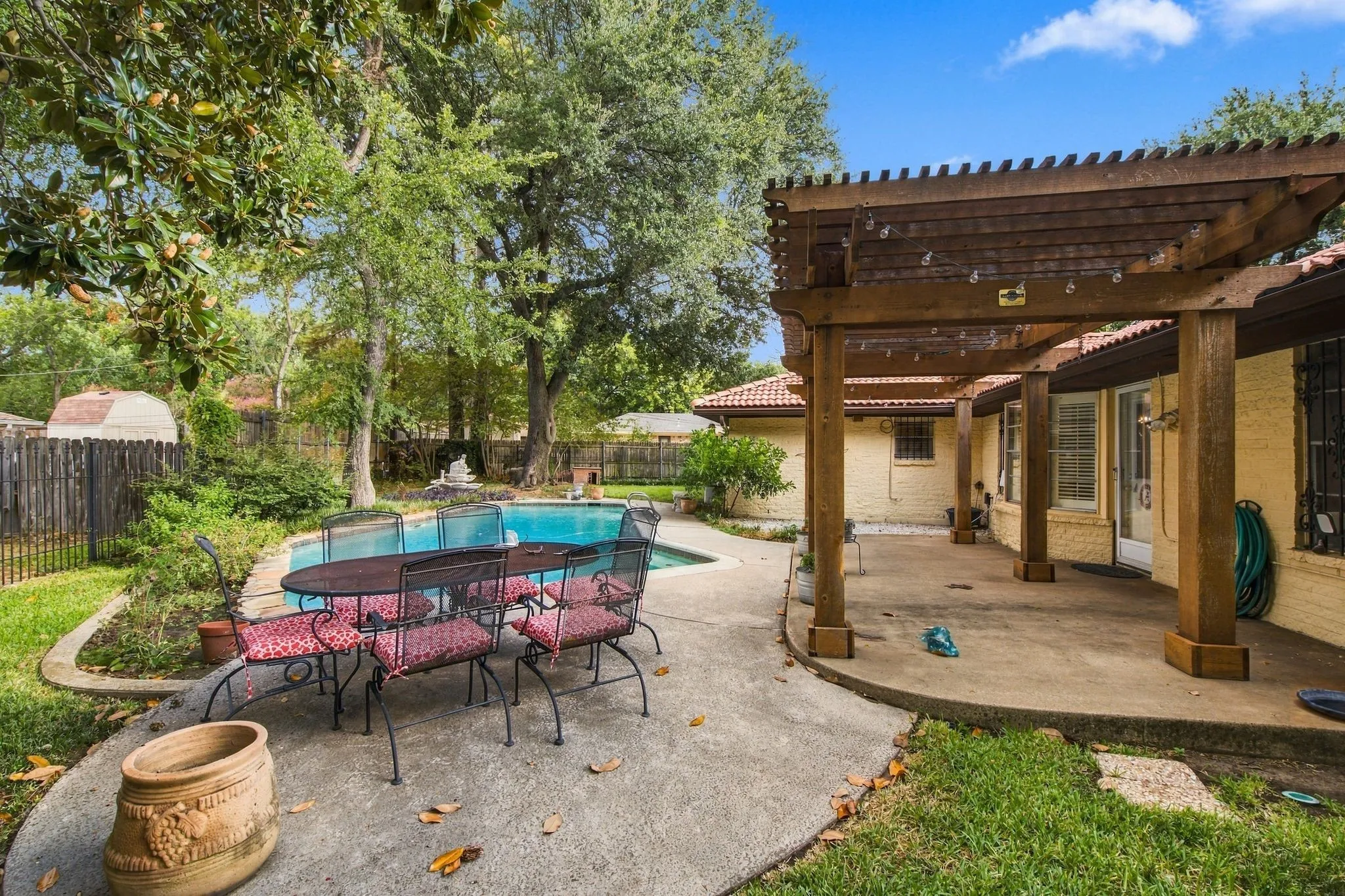 Curved concrete patio with a wooden pergola, an in-ground swimming pool, and mature trees