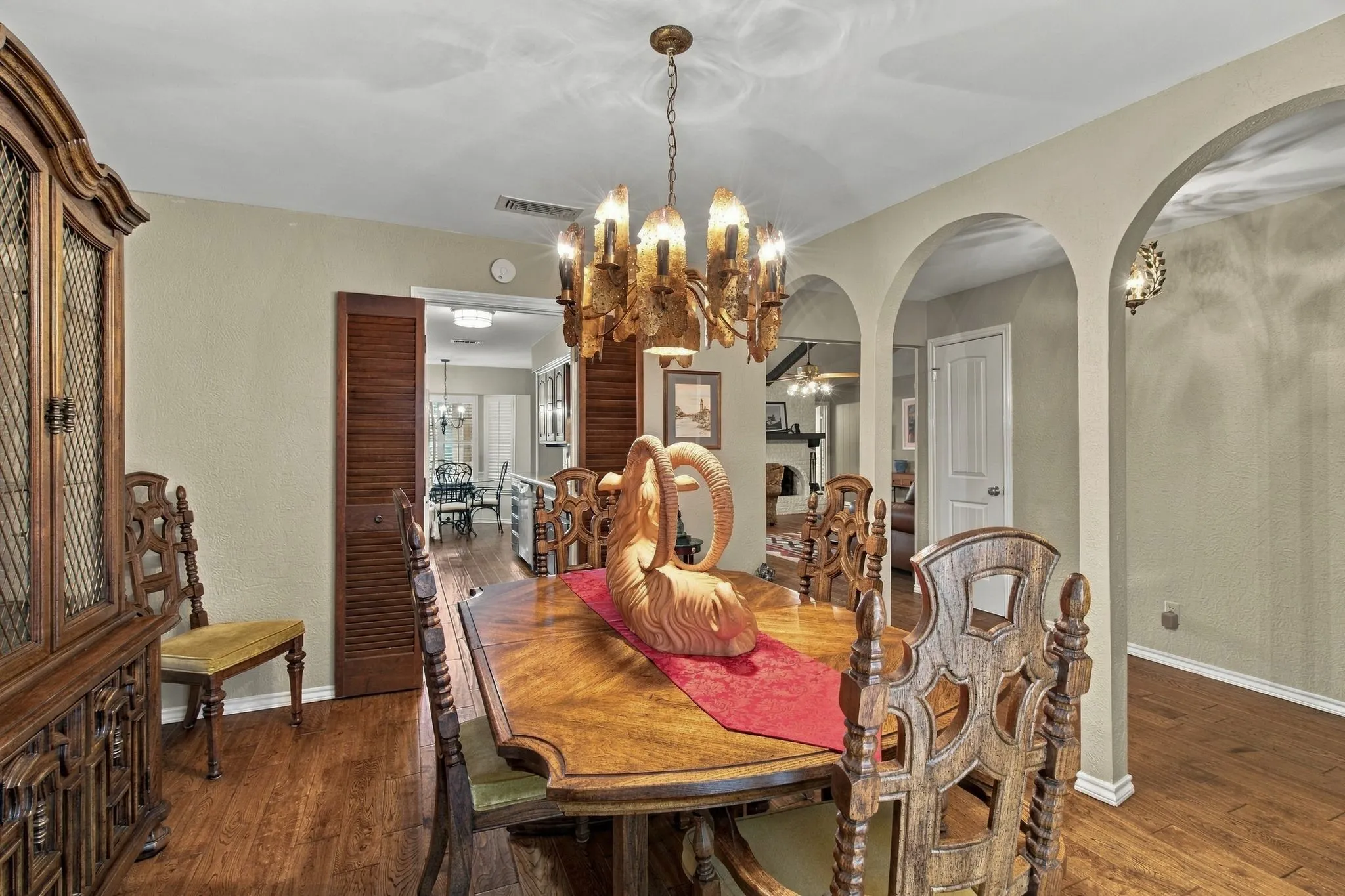 Wood-finish flooring throughout, featuring multiple arched doorways, and a prominent chandelier