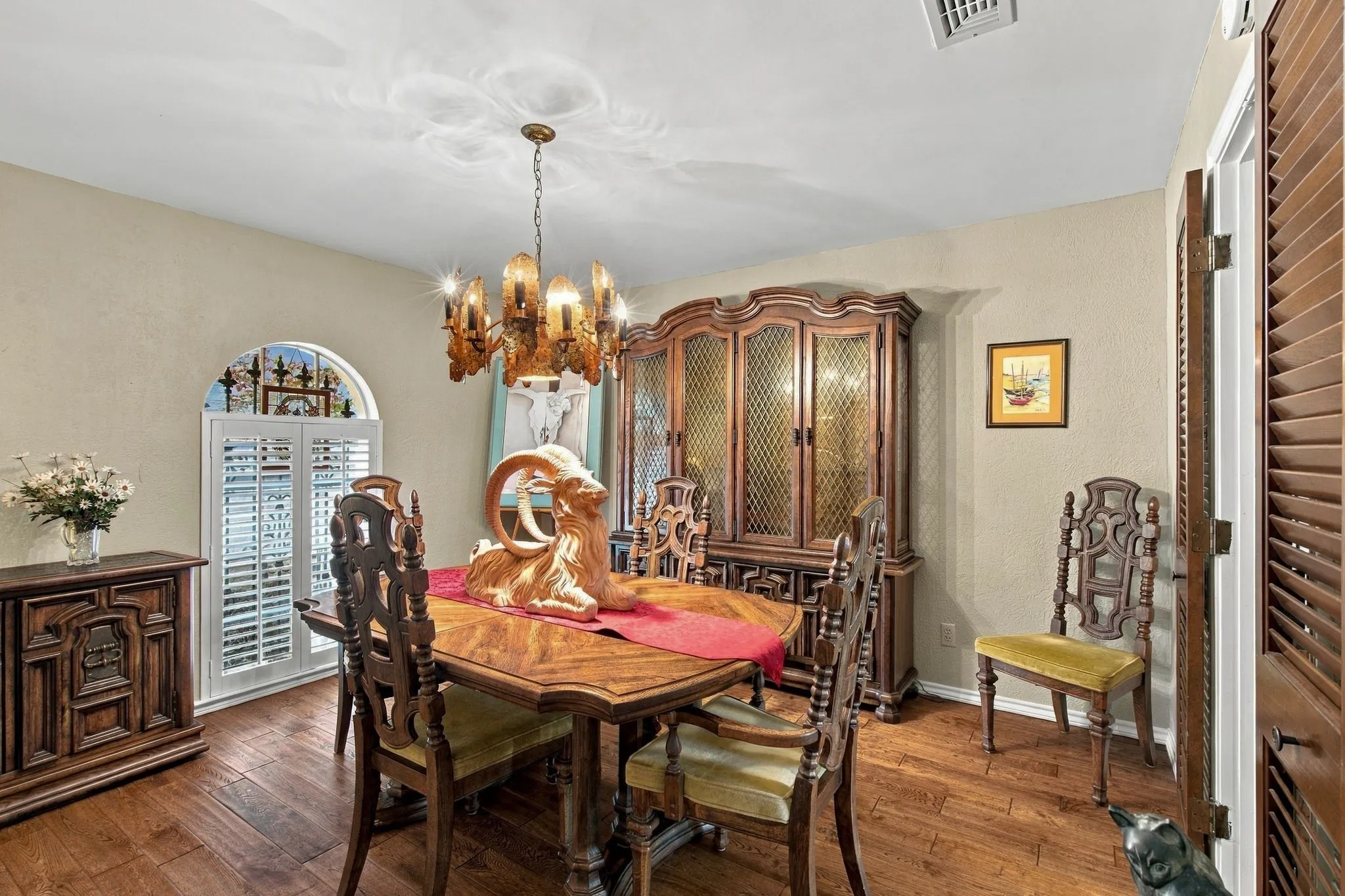 Wood-finish flooring, an arched window with white louvered shutters, and a brass chandelier