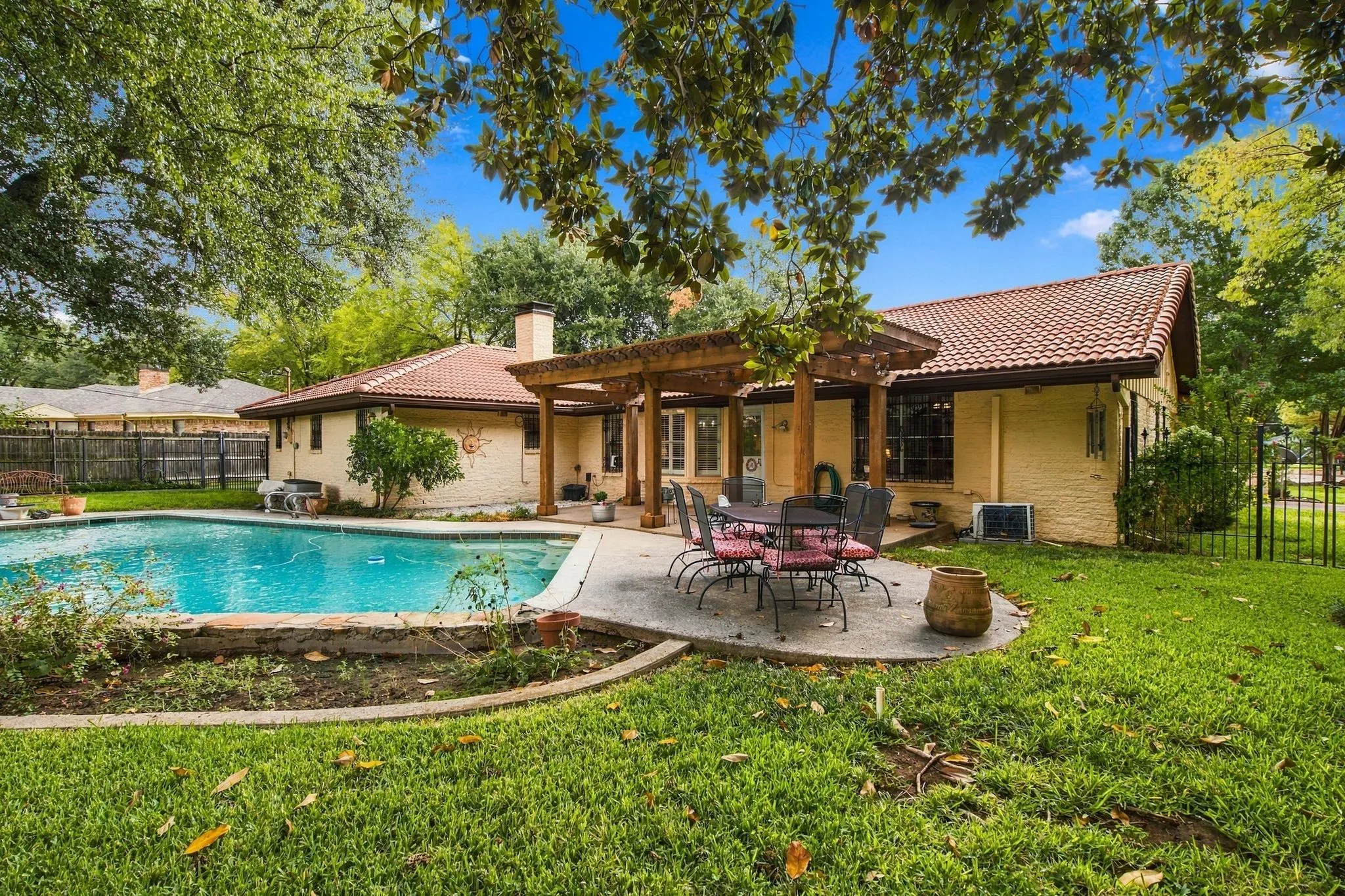 Expansive backyard featuring a swimming pool, concrete patio, wood pergola, and tile roof
