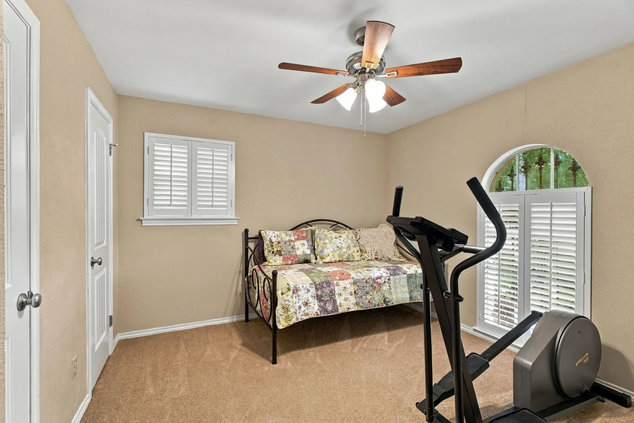 Carpeted room featuring a ceiling fan with integrated lighting, a rectangular window with white plantation shutters, and an arched window with white plantation shutters