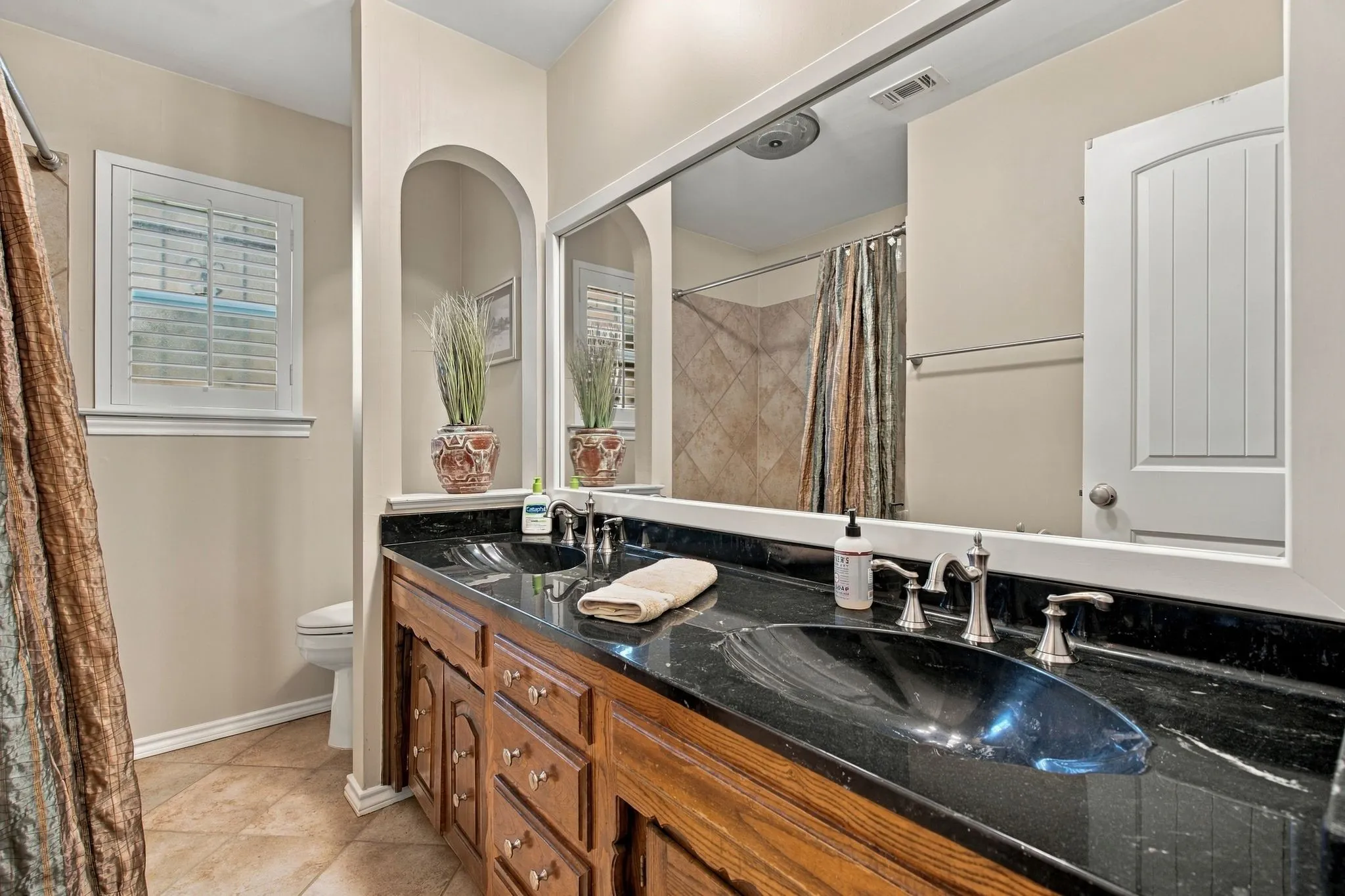 Dual vanity with dark stone countertop, wood-finish cabinetry, and brushed nickel fixtures