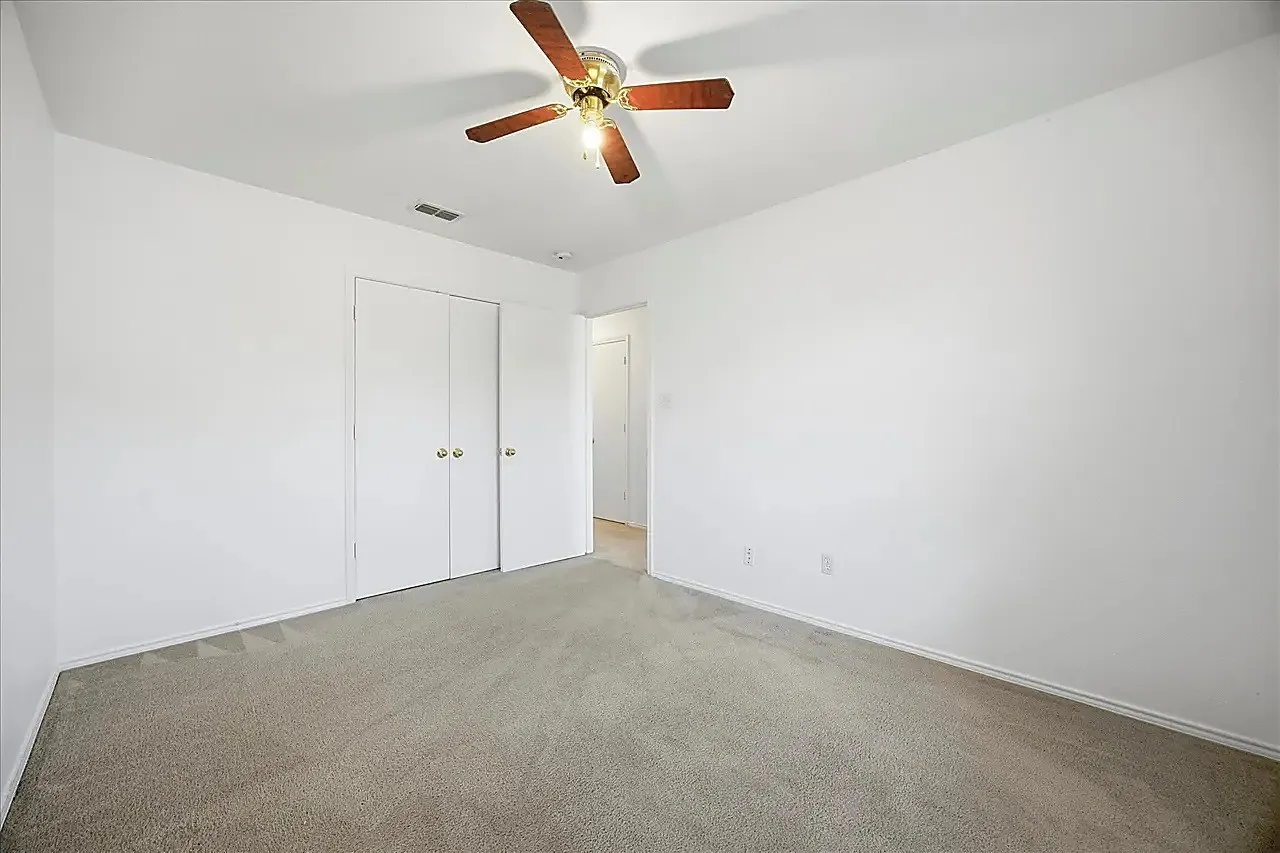 White walls, neutral carpet flooring, and a ceiling fan with integrated lighting