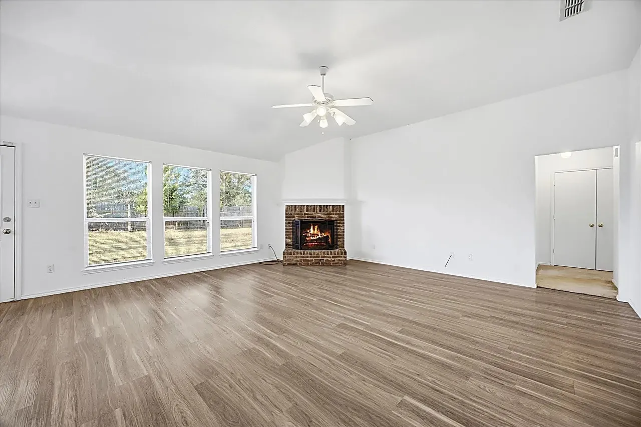 Spacious living area featuring wood-finish flooring, a brick fireplace, vaulted ceilings, and a ceiling fan