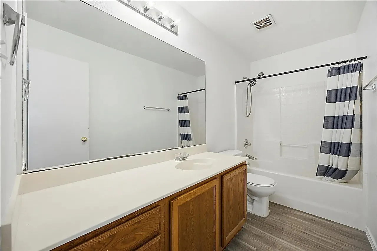 White vanity countertop with an integrated sink, wood-finish cabinetry, and a full-width mirror