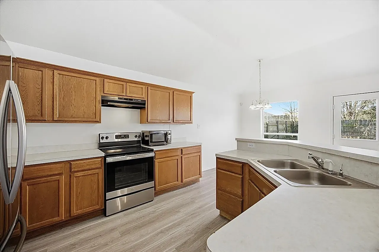 Kitchen featuring wood-finish cabinetry, stainless steel appliances, light-toned countertops, and wood-finish flooring