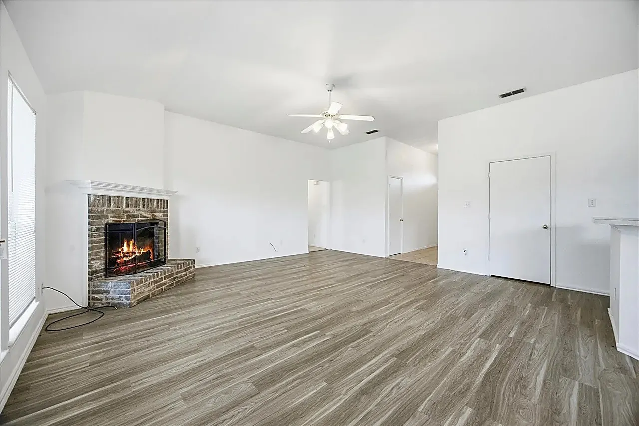 Spacious interior with wood-finish flooring, a brick-surround fireplace, and a ceiling fan