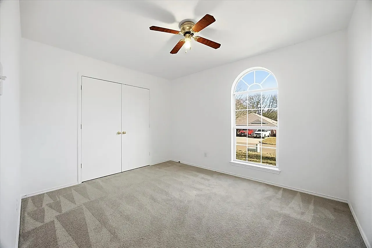 Arched window, carpet flooring, ceiling fan, and double bi-fold doors