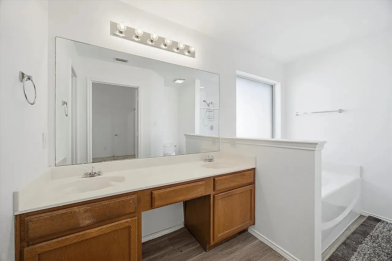 Double vanity with integrated sinks, expansive mirror, wood-finish cabinetry, built-in bathtub, and overhead light fixture
