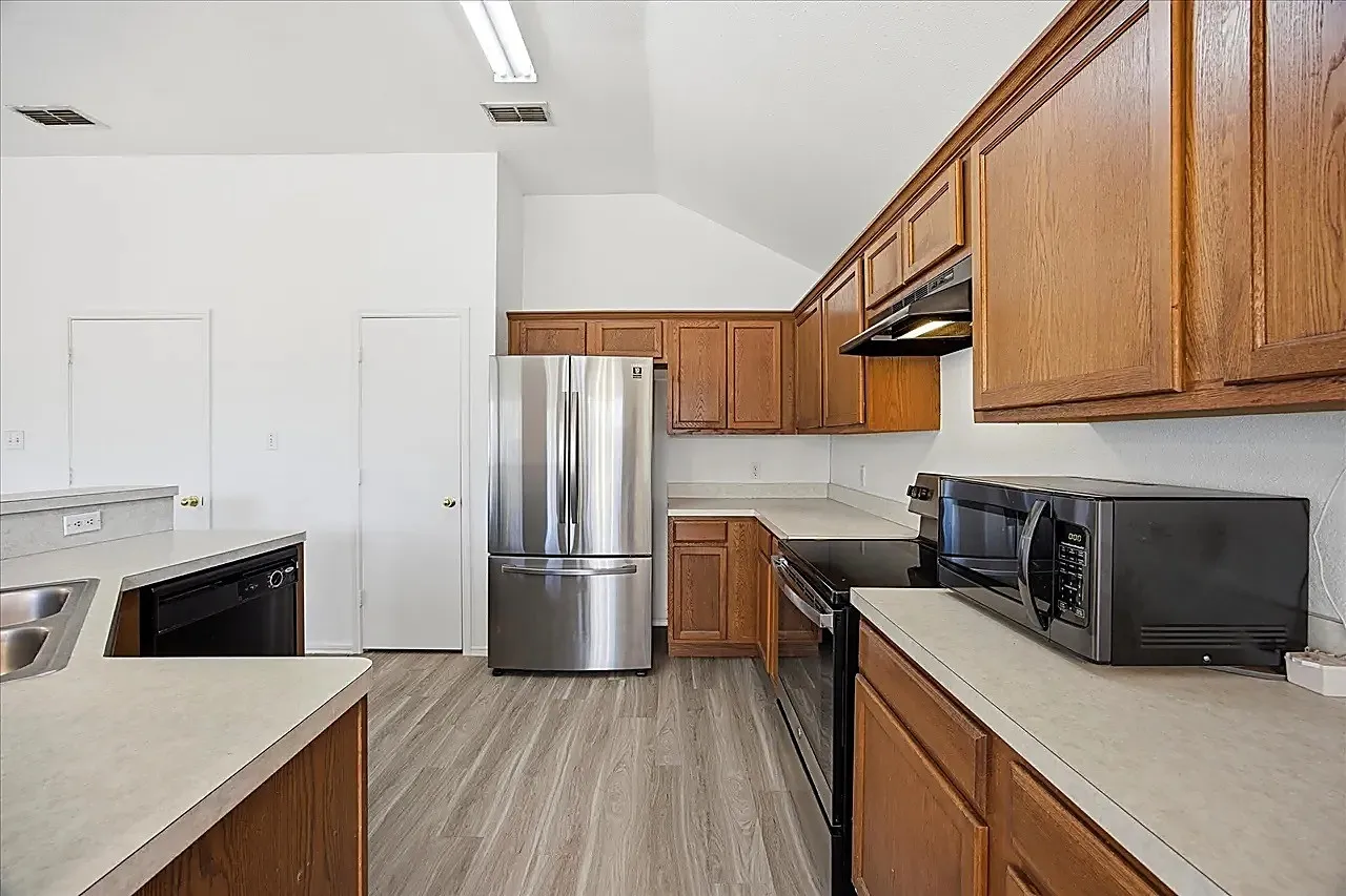 Kitchen featuring wood-finish cabinetry, stainless steel refrigerator, integrated dishwasher, light-toned countertops, and wood-finish flooring