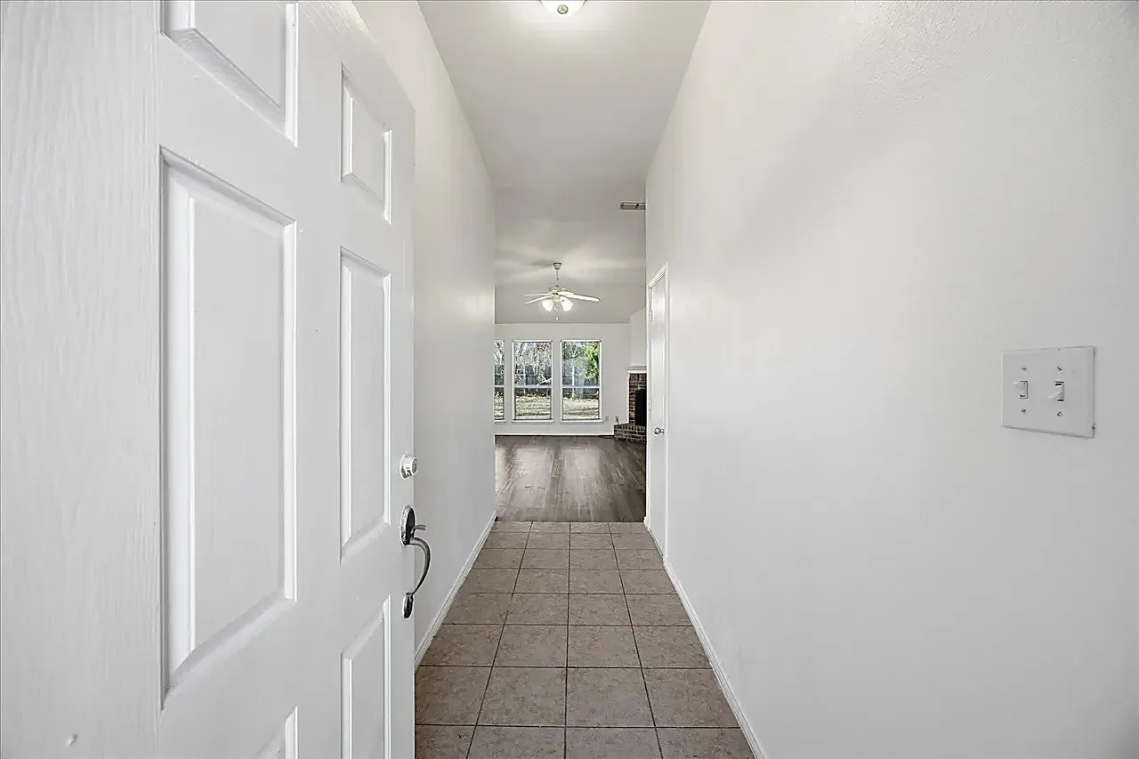 Entryway with tile flooring, leading to a living area with wood-finish flooring and multiple windows