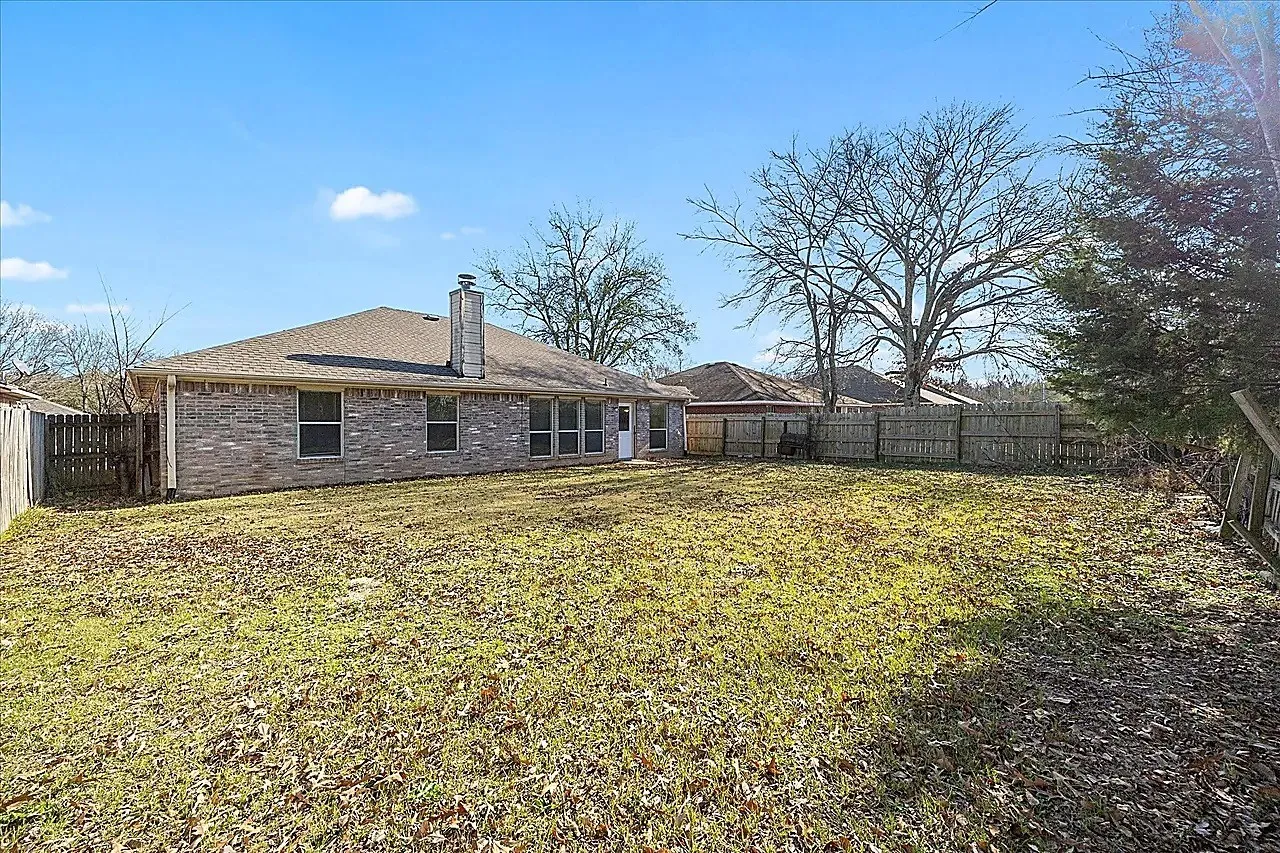 Expansive backyard featuring a partial wood fence, a brick exterior, multiple windows, and a rear door