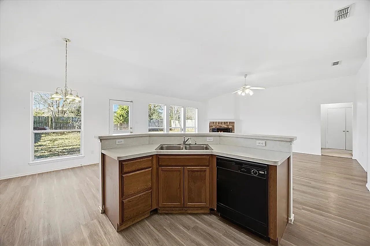 Open-concept living area featuring wood-finish flooring, vaulted ceilings, and a corner kitchen island with a double basin sink