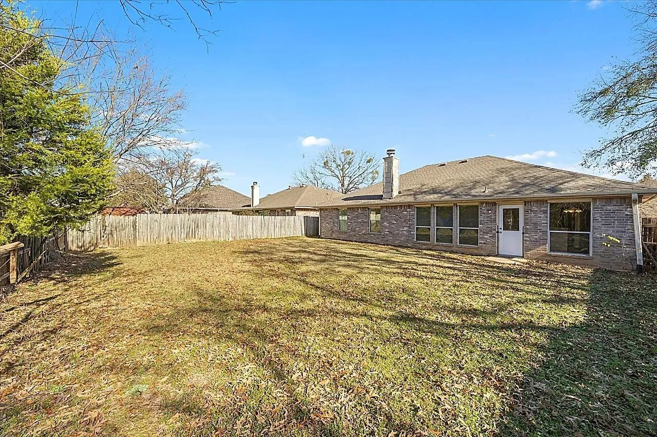 Expansive backyard featuring a wood fence, brick exterior, multiple windows, and a rear entry door