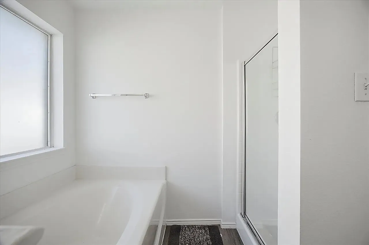 Modern bathroom featuring a soaking tub with chrome fixtures, frameless glass shower enclosure, white subway tile walls, and dark wood-finish flooring with integrated bath mat area