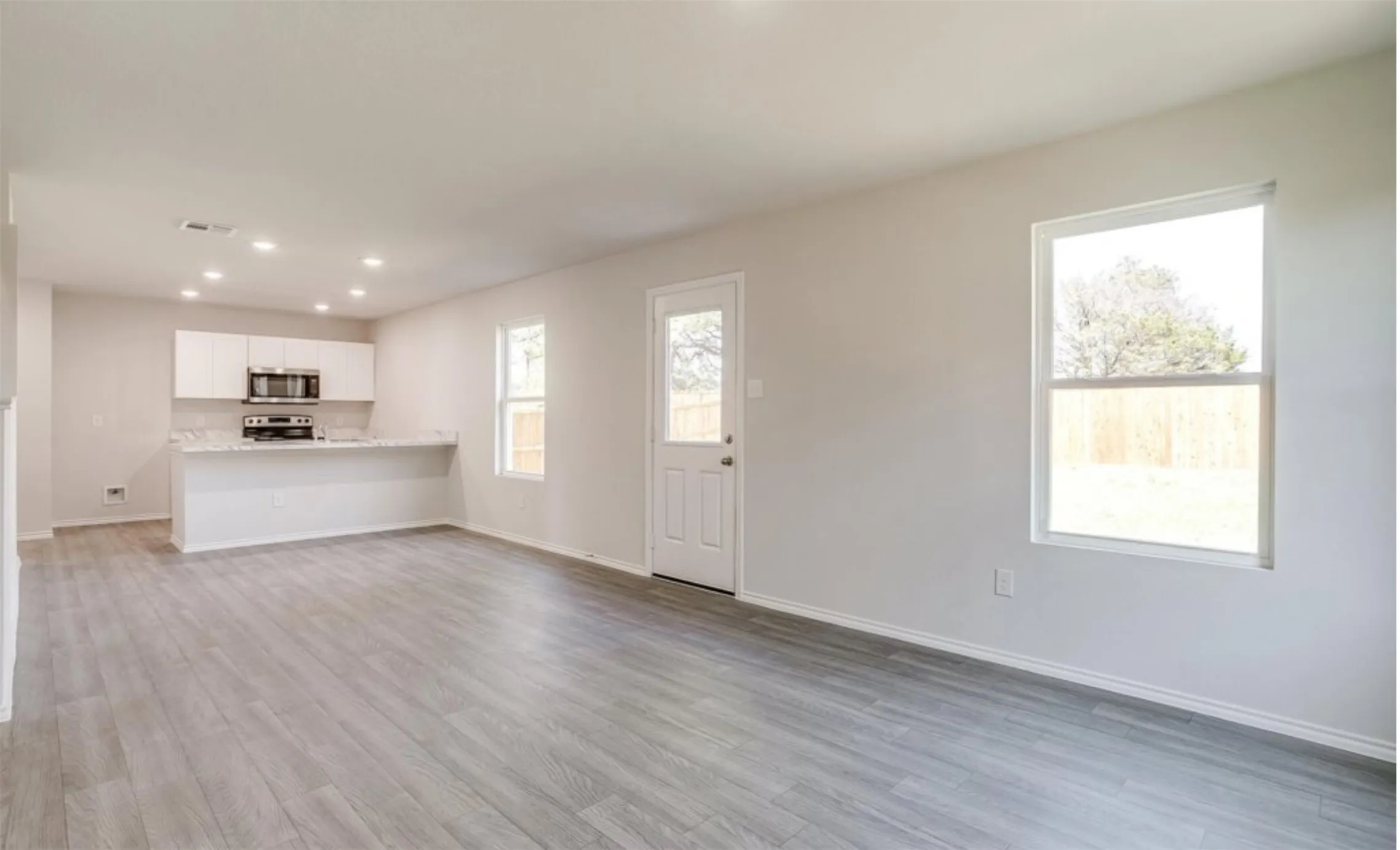 Open-concept living space featuring wood-finish flooring, recessed lighting, and a kitchen with white cabinetry, stainless steel appliances, and a breakfast bar