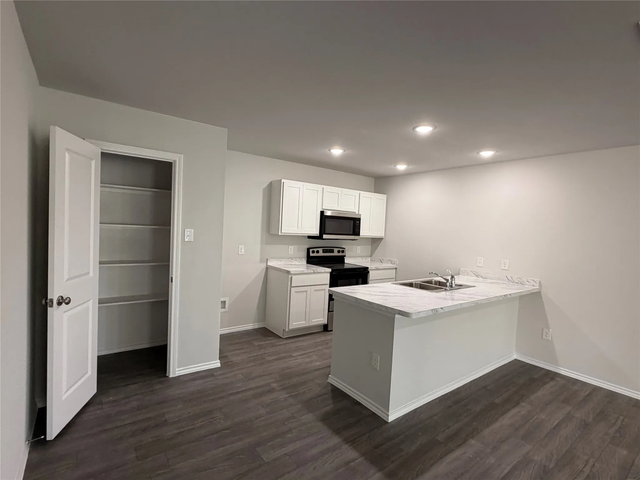 Kitchen featuring white shaker cabinetry, stainless steel microwave, stone-finish countertops, and wood-finish flooring