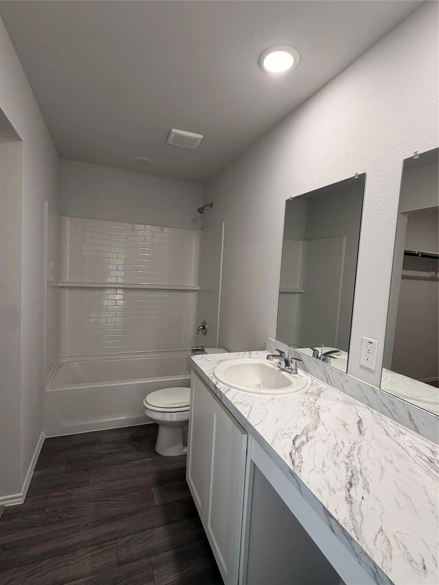 White subway tile shower surround, white vanity cabinetry, integrated single basin sink, laminate countertop, and wood-finish flooring